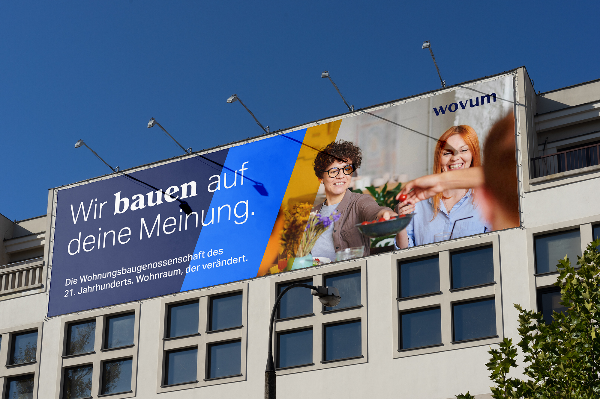 The image shows a photograph of a large wovum billboard in an urban setting.